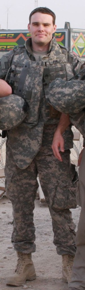 Jack Phillips in uniform and body armour, holding a helmet, in Afghanistan